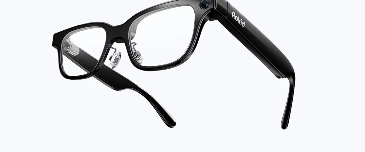 Black wayfarer-style smart glasses with a camera at the hinge, seen from three-quarter view